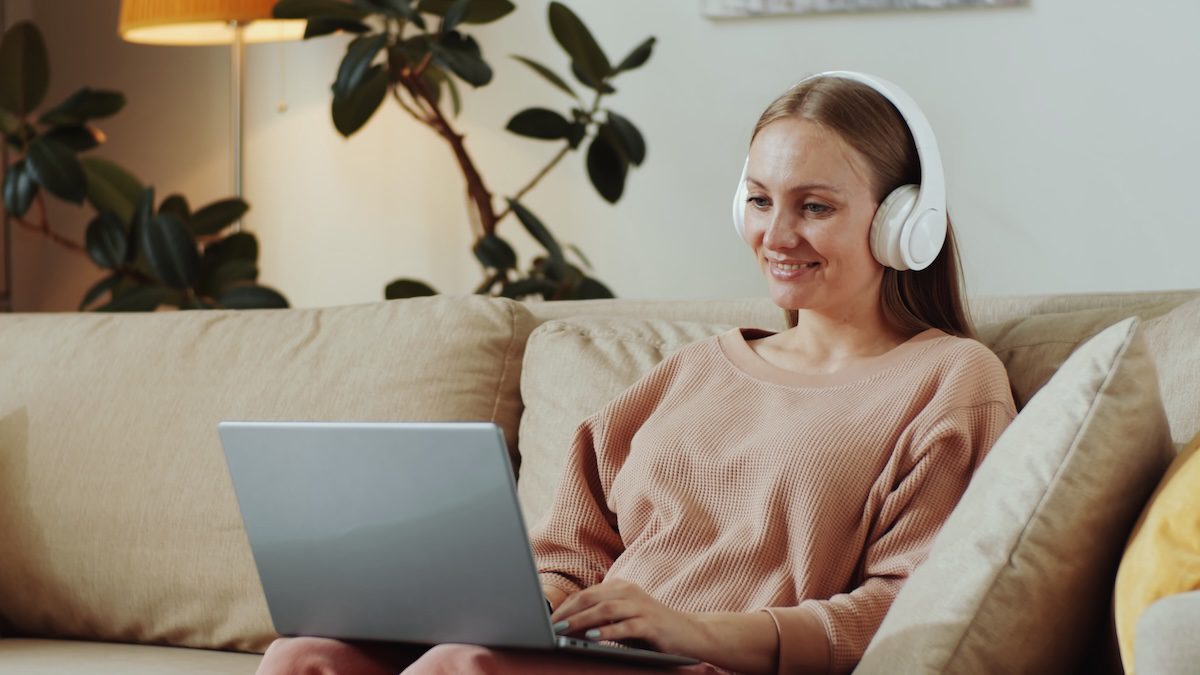 A B2B buyer watches video content on a laptop from her couch, headphones on and engage
