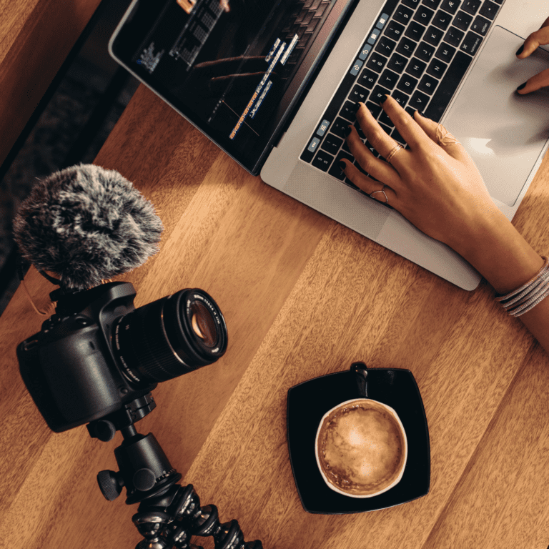 An video editor works on a computer with a dslr camera and coffee close by.